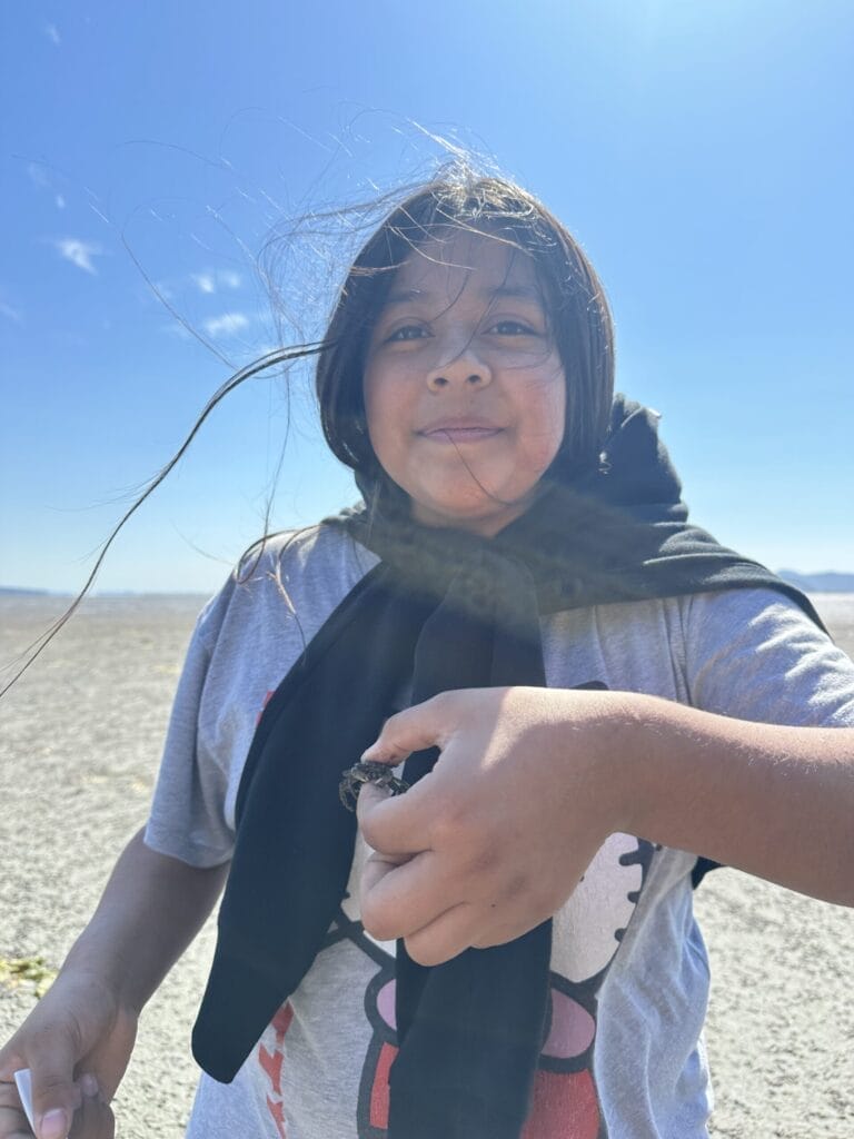 A girl holds a small crab on the beach.